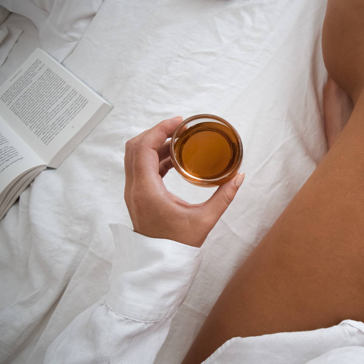 girl holding a glass of tea on a bed with white sheets