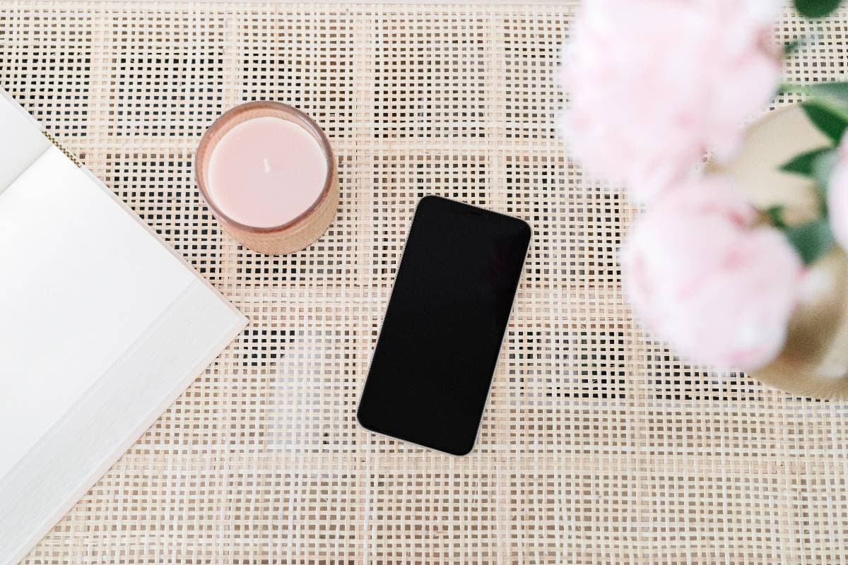 iphone on a rattan table with pink flowers and a pink candle